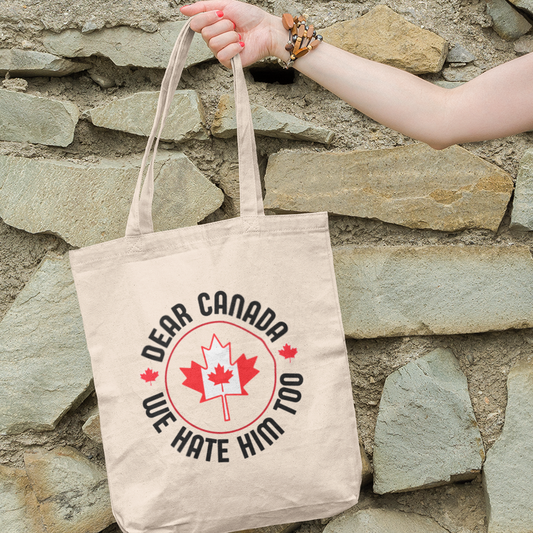 A person holding a natural-beige tote bag with text on it, standing against a stone wall background.